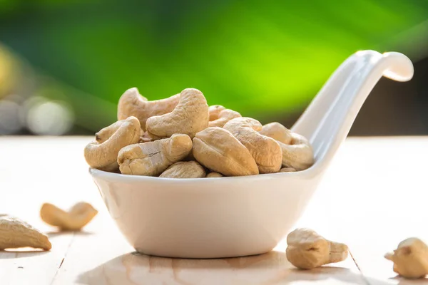 Geroosterde cashewnoten in witte kom op groene natuur achtergrond — Stockfoto