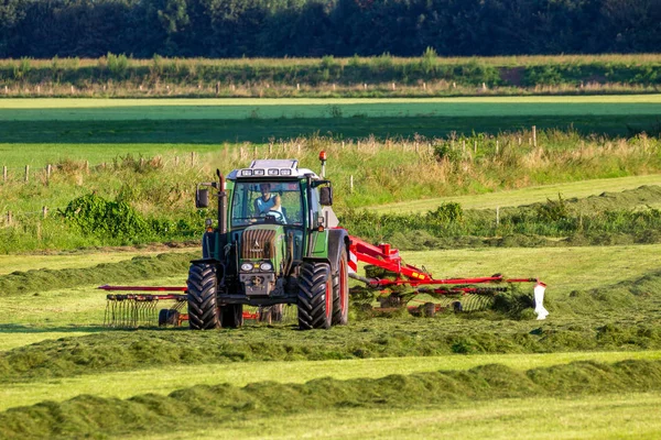 Agricultor usando un tractor Fendt para trabajar después de cortar hierba . — Foto de Stock
