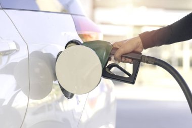 İnsan eli ve siyah yakıt hortumu beyaz bir arabaya benzin dolduruyor.