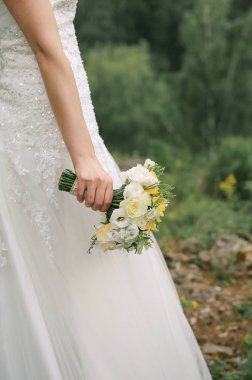 Gelin güzel beyaz ve sarı bir düğün buketi tutuyor.