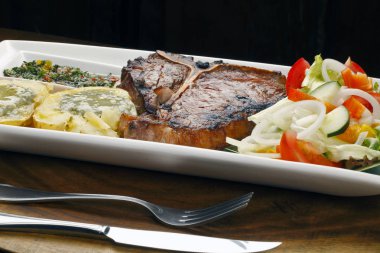 Kızarmış porterhouse veya t-bone biftek, patates ve salata ile ihale 