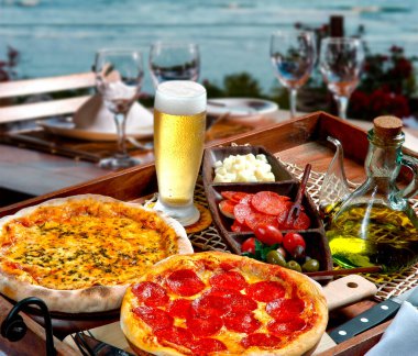 Pepperoni pizza, mozzarella, atıştırmalık ve arkada deniz olan soğuk bira.