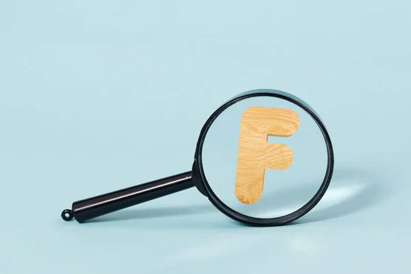 3D decorative wooden Alphabet, capital letter F throw Magnifying glass, on a pastel blue background — Stock Photo, Image