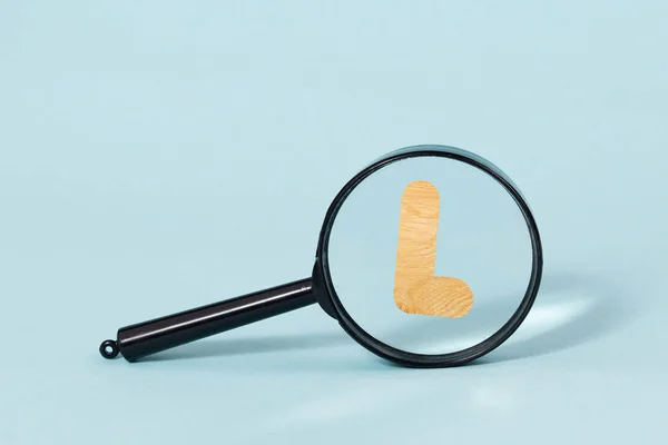 Alfabeto de madeira decorativo 3D, letra maiúscula L jogar lupa, em um fundo azul pastel — Fotografia de Stock
