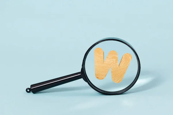 Alfabeto de madeira decorativo 3D, letra maiúscula W jogar lupa, em um fundo azul pastel — Fotografia de Stock