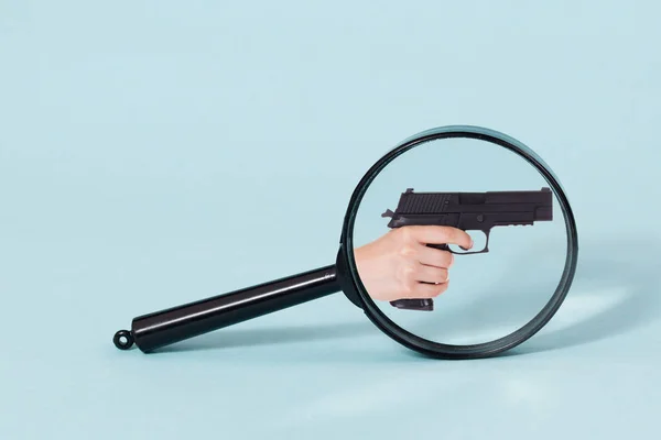 Gun handle throw Magnifying glass, on a pastel blue background — Stock Photo, Image