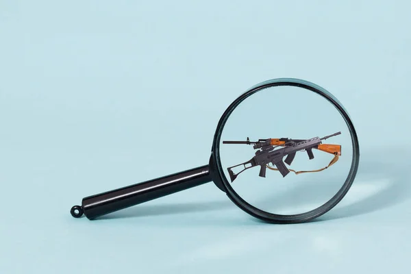 Two AK-47 assault rifles seen through a magnifying glass, isolated on a light blue background. — Stock Photo, Image