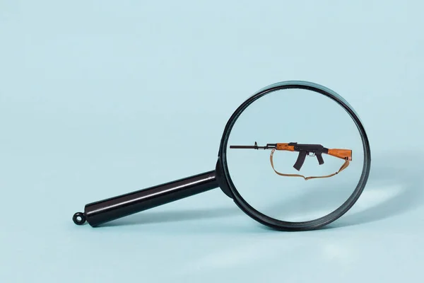 A shotgun under the magnifying glass on a light blue background. — Stock Photo, Image