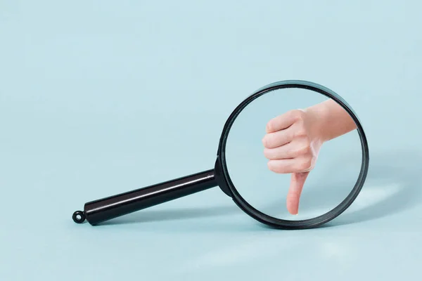 Hand with thumb down throw Magnifying glass, on a pastel blue background — Stock Photo, Image