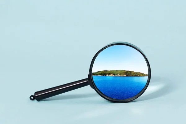 Une île dans la mer sous une loupe sur fond bleu clair . — Photo