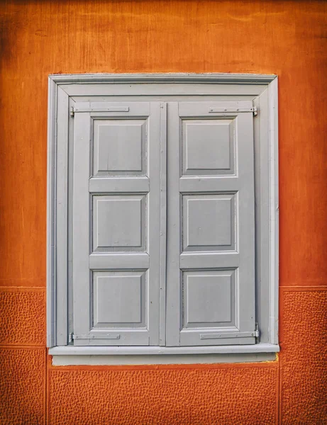 Grey shutters window on vibrant orange wall — Stock Photo, Image
