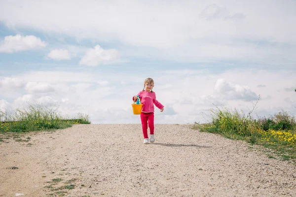 Mavi kürek ve sarı kovayla oynayan gözlüklü kız.