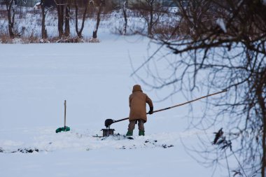 unidentified fisherman puts mud in a metal sieve to wash out bloodworm to use it as bait for predator fishing, little, natural, frozen winter lake, outdoor active hobby