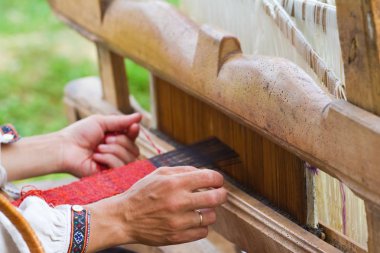 Ukrayna 'nın geleneksel vyshyvanka tişörtündeki deneyimli kadın sanatçının elleri antik dokuma tezgahında parlak renkli yün ipliklerden bir halı örüyor.