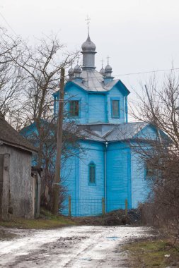 Prybuzke, Ukraine - 04.02.2020: muddy dirt road lead to Assumption of Mary russian Orthodox church, wooden temple with blue walls, religious believer tourism