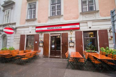 Viyana, Avusturya - 05.05.2019: Geleneksel tarzda küçük restoran Wiener Kueche beim Hofmeister, Braunerstrasse, Wien Şehir Merkezi, yağmurlu bir pazar sabahı kapalı, dışarıda ziyaretçi yok, masalar ve sandalyeler yağmur damlalarıyla ıslanmış.
