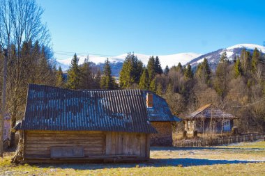 Döşeme çatılı eski ahşap ahır, Mart sabahı çimlerin üzerinde beyaz don, Karpat Dağları 'nın Zakarpattia bölgesi için tipik geleneksel mimari, turist keşfi konsepti