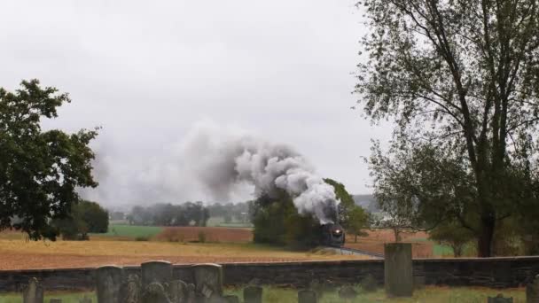 墓地から見える霧の雨の日に煙と蒸気で貨物を引く蒸気機関車 — ストック動画