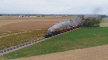 Strasburg, Pennsylvania, Ekim 2019 - Güneşli bir günde antika yolcu arabalarını çekerken, buhar ve duman püskürten bir buhar makinesinin havadan görüş açısı