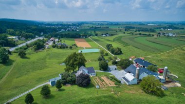 Güneşli bir kırsalda, güzel bir gökyüzünde büyüyen yeşil tarlaların ve yuvarlanan ekinlerin havadan görünüşü.