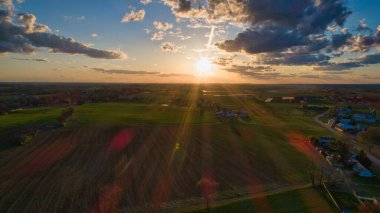 Mavili gökyüzü, bulutlar ve kızıl güneşli altın saat boyunca ahırlar, silolar ve tarım arazilerinin üzerindeki günbatımının havadan görünüşü