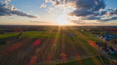 Mavili gökyüzü, bulutlar ve kızıl güneşli altın saat boyunca ahırlar, silolar ve tarım arazilerinin üzerindeki günbatımının havadan görünüşü