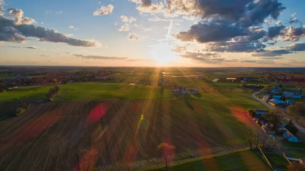 Mavili gökyüzü, bulutlar ve kızıl güneşli altın saat boyunca ahırlar, silolar ve tarım arazilerinin üzerindeki günbatımının havadan görünüşü