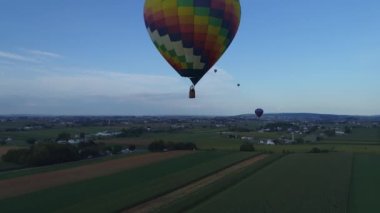 Pensilvanya kırsalında güneşli bir yaz günü öğleden sonra bir festival sırasında çiftliklerde yüzen sıcak hava balonları.