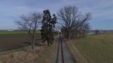 Yenilenmiş bir buharlı lokomotifin dumanı ve tren çiftliğinin arkasından duman ve buhar üfleyen yolcu arabalarının hava görüntüsü.