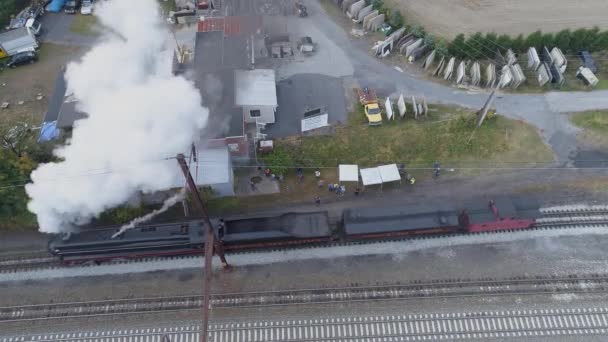 黒い煙と蒸気を吹いているのを見て観客と貨物ヤードを通過するアンティーク復元された蒸気機関車の頭の上に空中 — ストック動画