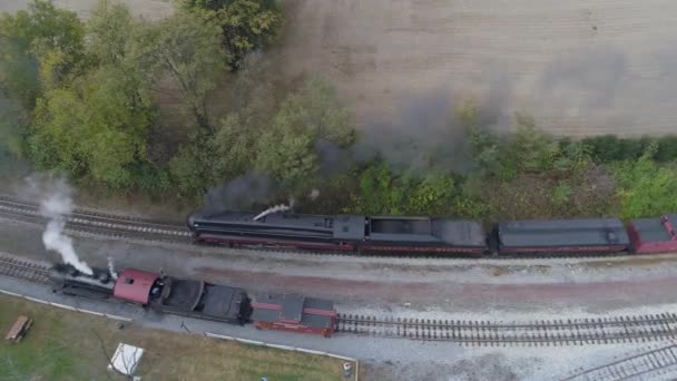 黒い煙と蒸気を吹いている2つのアンティーク復元された蒸気機関車が貨物ヤードを通って移動する空中 — ストック動画