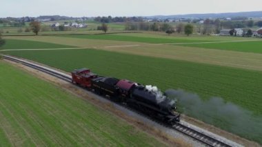 Strasburg, Pennsylvania, Ekim 2019 - Buharlı lokomotifi restore ederek siyah beyaz duman ve buhar üflerken kırsal alanda geriye doğru giden hava görüntüsü