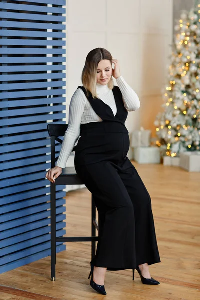 Jeune femme enceinte brune en combinaison noire sur fond d'arbre de Noël. Grossesse mode . — Photo