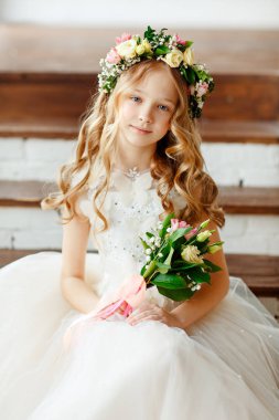 Şirin bir çocuk. Pembe elbiseli ve çiçek taclı bir kız. Parlak bir stüdyoda oturan güzel küçük kız kameraya bakar ve elinde bir buket taze çiçek tutar..