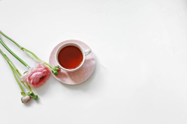 Beyaz arka planda izole edilmiş bir fincan çay ve pembe çiçek manzarası. Düz, romantik bir kadın sabahı.