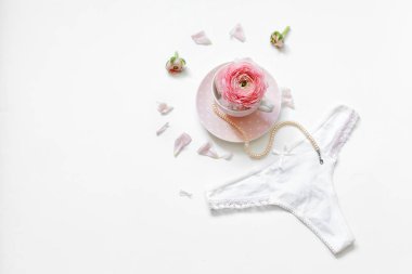 Bir fincan çay, çiçek yapraklarının yanında bir dizi inci ve beyaz arka planda kadın tangası vardı. Mesaj için yer. Minimum kadın aksesuarları.