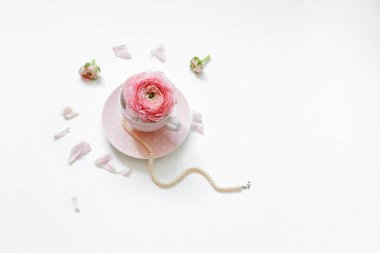 Beyaz arka planda çiçek yaprakları olan bir dizi inciyle bir fincan çay yatıyordu. Mesaj için yer. Minimum kadın aksesuarları.