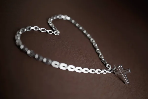 Cruz cristiana de plata y cadena sobre fondo marrón con símbolo del corazón . —  Fotos de Stock