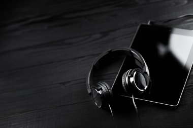 Dijital tablet ve koyu ahşap bir masa üzerinde kulaklık.