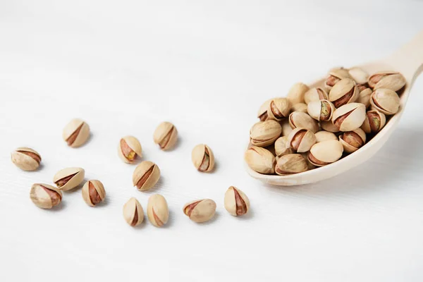 Pistachos sobre cuchara de madera sobre fondo de madera blanca. Primer plano — Foto de Stock