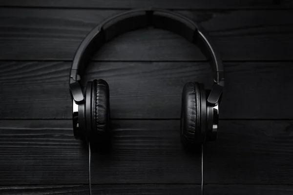 Black headphones on black wooden dark background.