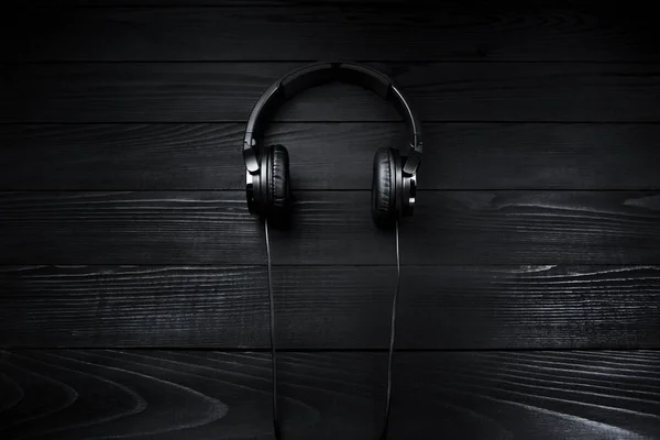 Black headphones on black wooden dark background.
