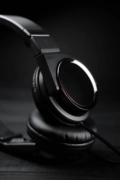 Black headphones on black wooden dark background.