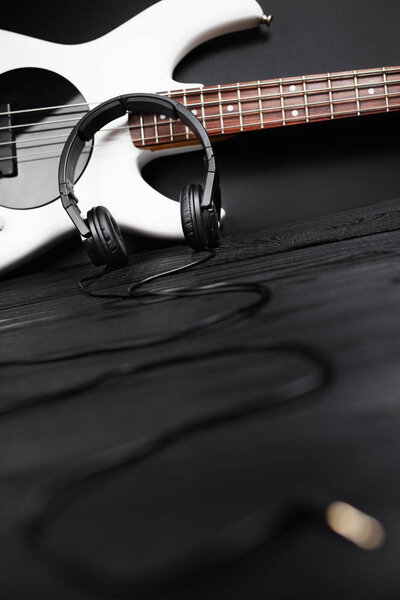 Black headphones and white bass guitar on the black wooden background