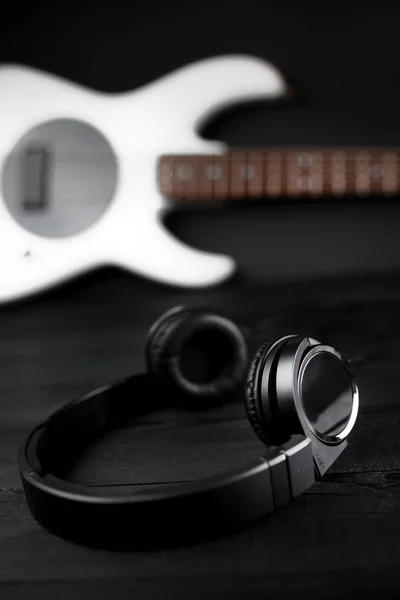 검은 나무 배경에 검은 헤드폰 및 화이트 베이스 기타. — 스톡 사진