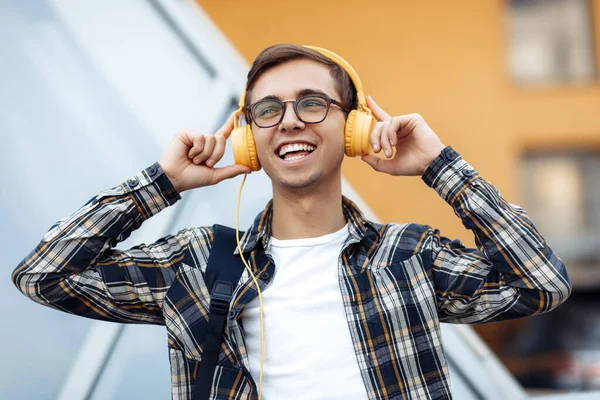 Knappe jonge mannelijke student in casual outfit met gele koptelefoon luisteren muziek op straat. — Stockfoto