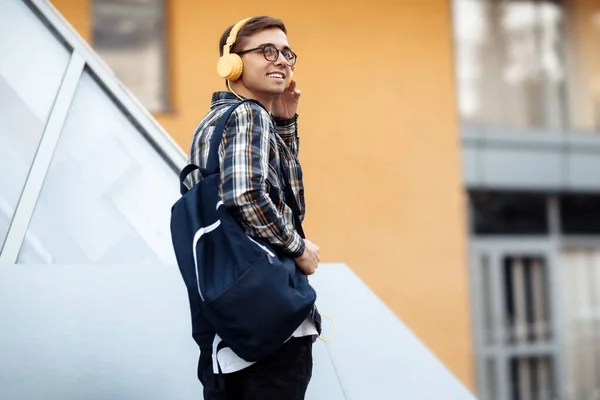 Jasny młody student w stroju casual z żółtymi słuchawkami słuchanie muzyki podczas spaceru po ulicy. — Zdjęcie stockowe