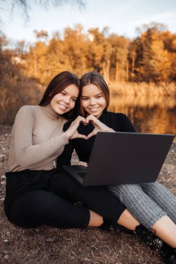 Parlak gülüşlü iki genç kız kardeş parkta aşk jesti yaparken dizüstü bilgisayar ya da not defteri kullanın.