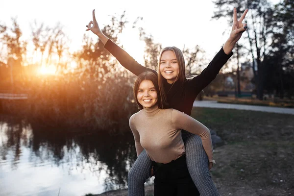 Positive two young twin sisters in casual outfit with bright smile posing at the park. Freedom concept.