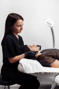 Kozmetik uzmanı, kozmetoloji merkezindeki siyah noktalardan ve sivilcelerden alınan çelik aletlerle derinin temizlenmesi için prosedür uyguluyor..